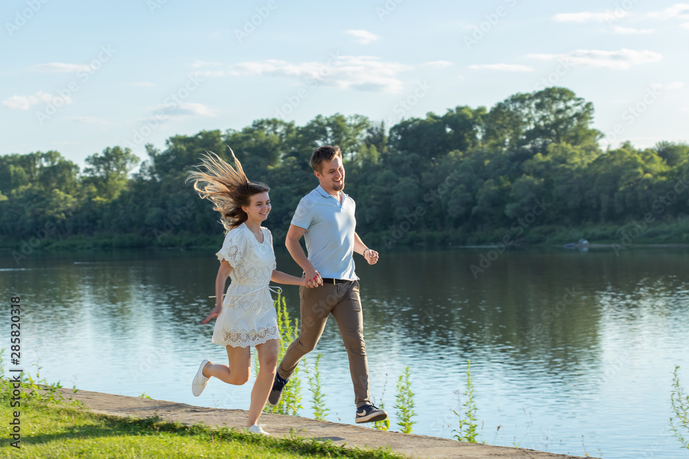 Summer nature, relationship and people in love concept - happy couple running near the lake Summer nature, relationship and people in love concept - happy couple running near the lake