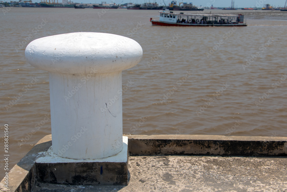 A shore with a white bollard and ferry on background.