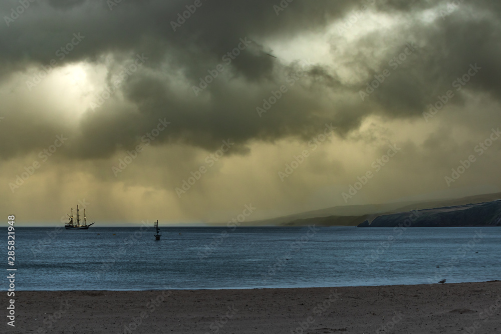 Dramatic stormy sunset whith tall ship at anchor in bay