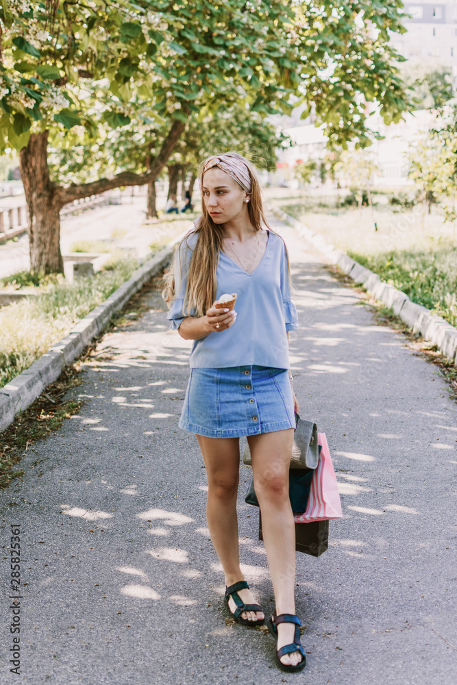 Summer city lifestyle girl portrait. Stylish young woman with ice cream in a waffle cone in her hand on a sunny summer hot day