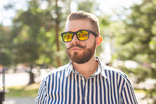 Portrait of a positive cheerful young man walking in the park on a warm sunny summer day. The concept of rest after study and work on weekends.