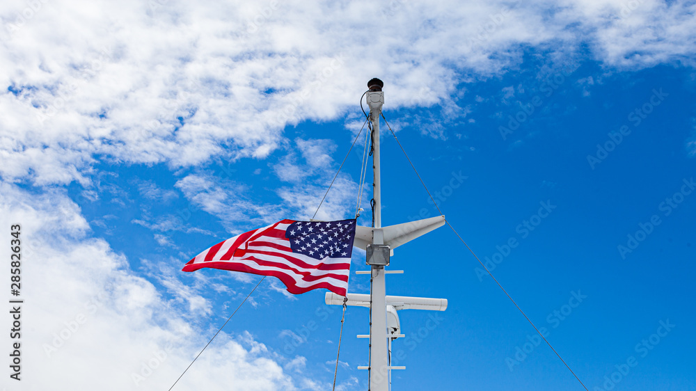 american flag flying off of boat in front of blue sky american flag flying off of boat in front of blue sky