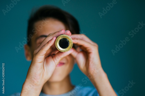 Cuadro en lienzo Close up of smiling boy looking at spyglass on blue background