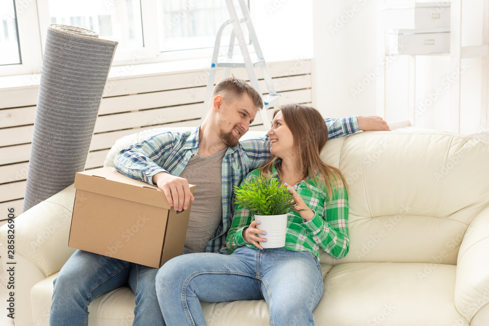 Positive cheerful couple rejoices in moving their new apartment sitting in the living room with their belongings. Concept of housewarming and mortgages for a young family.
