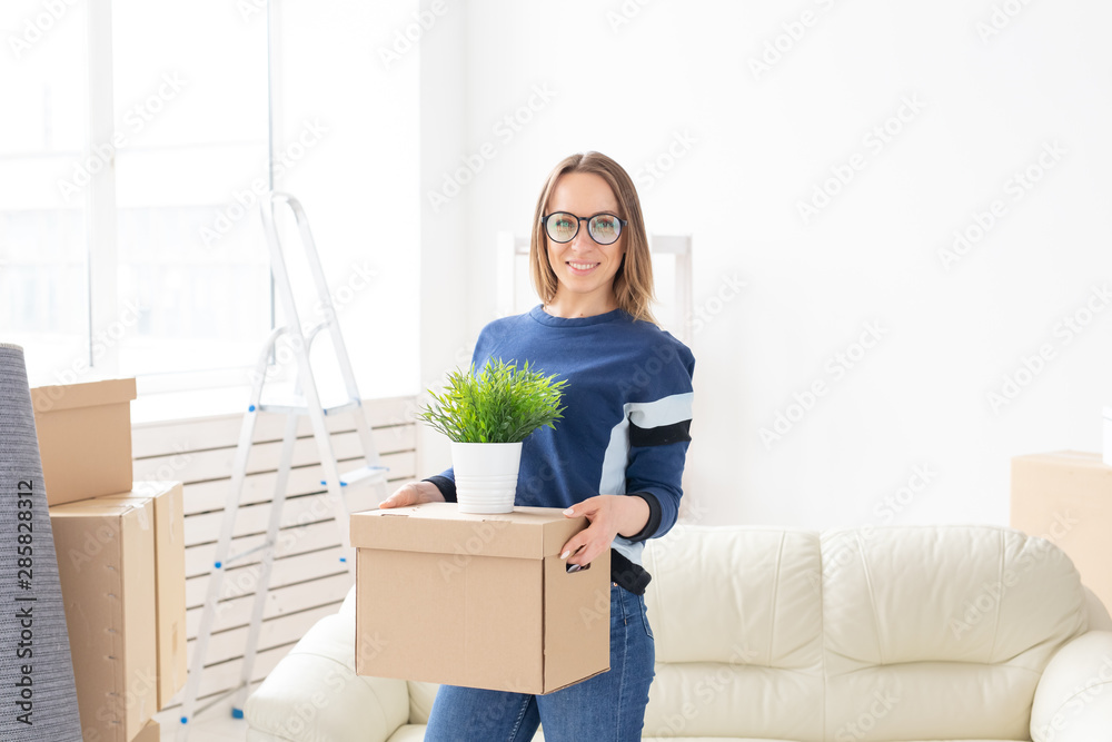 Young woman holds a box and a pot of plants while moving to a new apartment. Housewarming and new housing concept.
