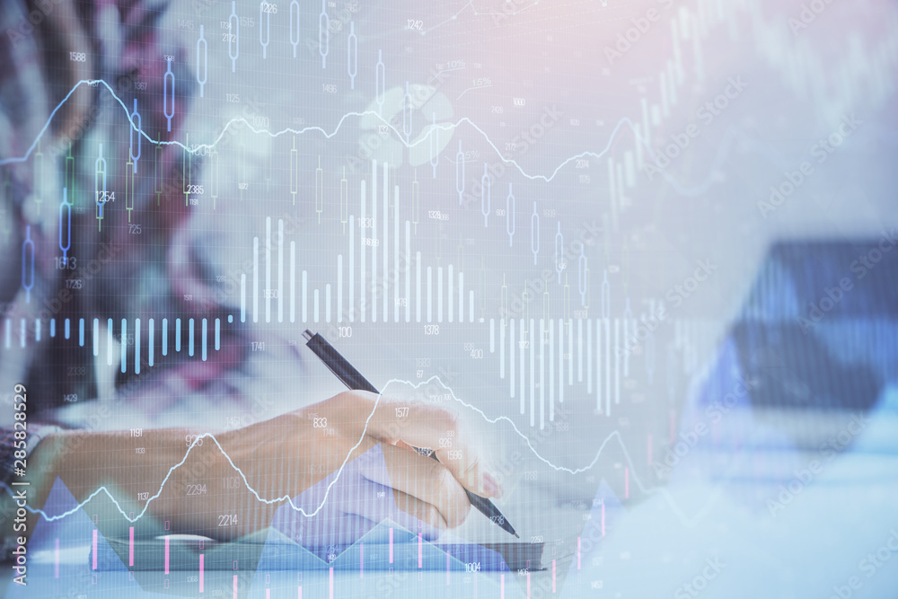 A woman hands writing information about stock market in notepad. Forex chart holograms in front. Concept of research. Double exposure A woman hands writing information about stock market in notepad. Forex chart holograms in front. Concept of research. Double exposure