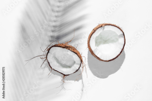 Minimalistic tropical still life. Halves coconut with shadows from palm leaves on white background. Creative fashion concept. Top view.