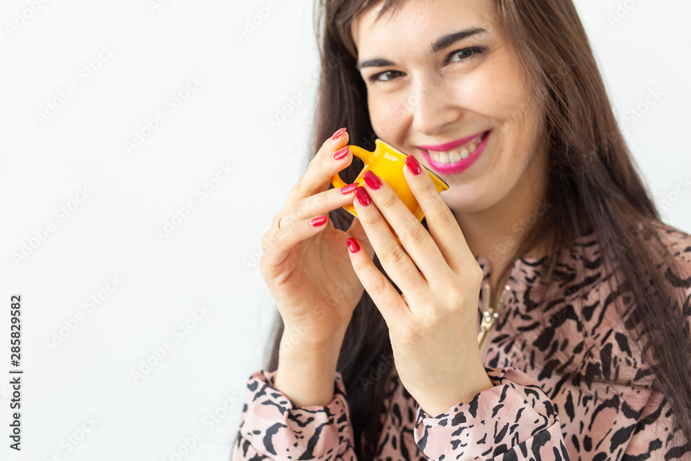 Playful young brunette woman holding in her hands a small yellow mug posing on a white background. Concept of morning coffee. Playful young brunette woman holding in her hands a small yellow mug posing on a white background. Concept of morning coffee.