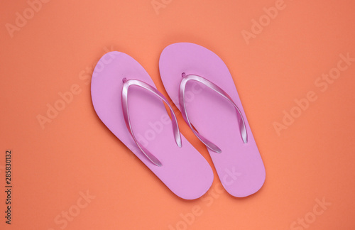 Trendy beach pink flip flops on coral paper background. Top view