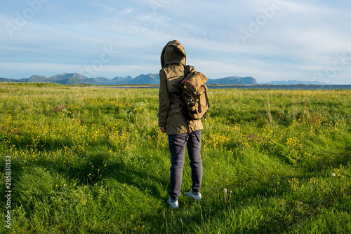 Girl in jacket with a hood and backpack enjoys scenic view. Beautiful nature landscape. Green grass, mountain. Lonely women. Enjoy moment, relaxation. Wanderlust. Travel and adventure. Explore Norway © Iuliia Pilipeichenko