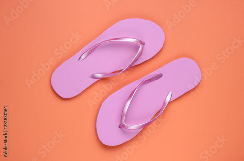 Trendy beach pink flip flops on coral paper background. Top view