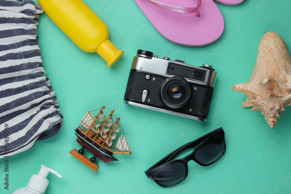 Summer still life. Beach accessories. Fashionable pink flip flops, bag, retro camera, sunblock bottle, sunglasses, seashell on blue paper background. Flat lay. Top view Summer still life. Beach accessories. Fashionable pink flip flops, bag, retro camera, sunblock bottle, sunglasses, seashell on blue paper background. Flat lay. Top view