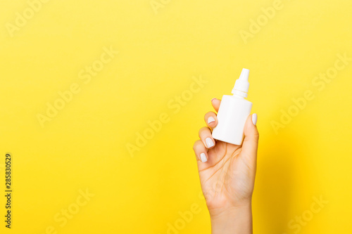 Female hands hold medicine bottle nose spray on yellow background isolation