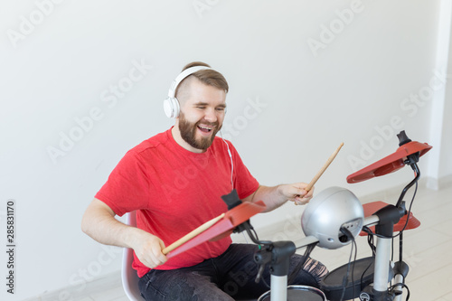 People, music and hobby concept - Man with white headphones playing the drums set over light background