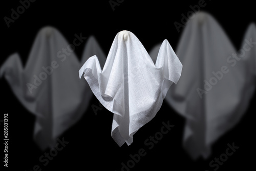 Photo of three halloween ghosts made of white fabric on black background.