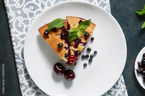 Piece of pie with blueberries, rasberry and mint for dessert on a white plate, napkin. Pieces of delicious homemade cake on a background