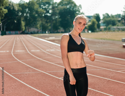 Young cheerful woman runner in sportswear on red-coated stadium outdoors