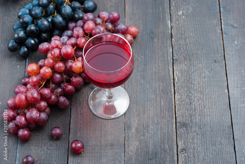 glass of red wine and grapes on black wooden table background