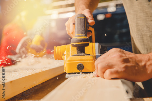 Male hands worker hold electric work planer with wooden board, smooth dust photo
