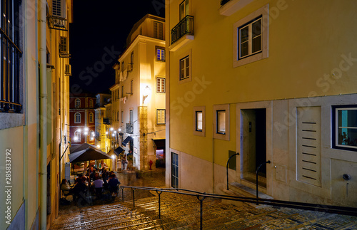 Lisbon, Portugal. Nighttime streets with stone stairs and restaurants under street lamps with evening illumination. Old downtown city centre.
