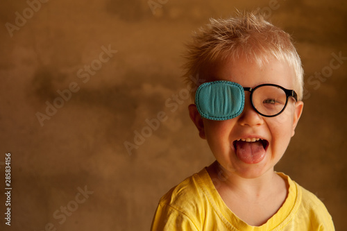 Portrait of funny child in new glasses with patch for correcting squint .Ortopad Boys Eye Patches nozzle for glasses for treatment of strabismus (lazy eye) photo