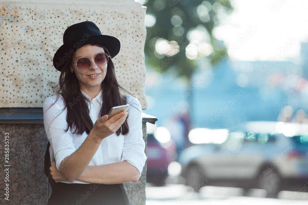young woman in a hat and with a backpack walks in the city and uses a smartphone.