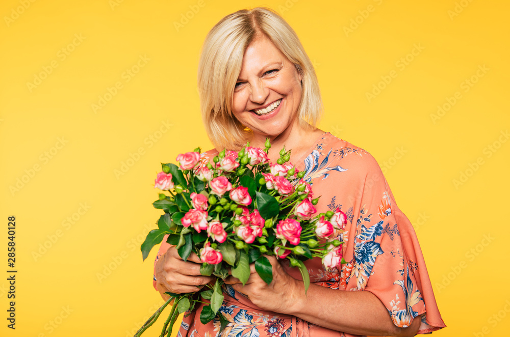 Holiday event. Mother's day. St. Valentines day. Birthday. Portrait of happy cute lovely senior woman in party colorful clothes with large bouquet of flowers on yellow background