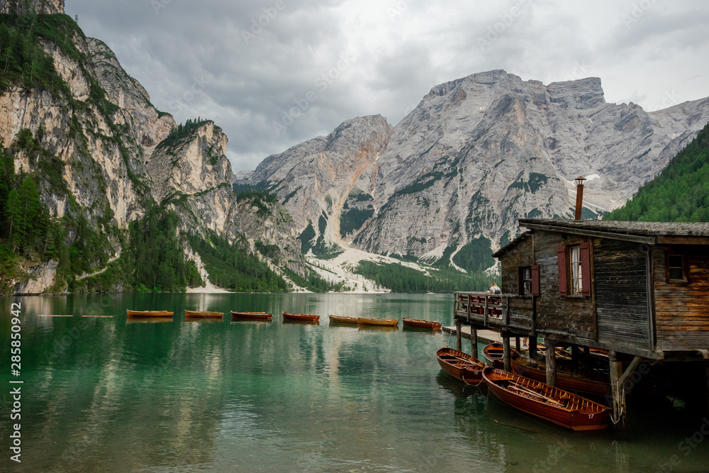 un chalet sur pilotis avec des barques , au bords des d'un lac vert devant des montagnes