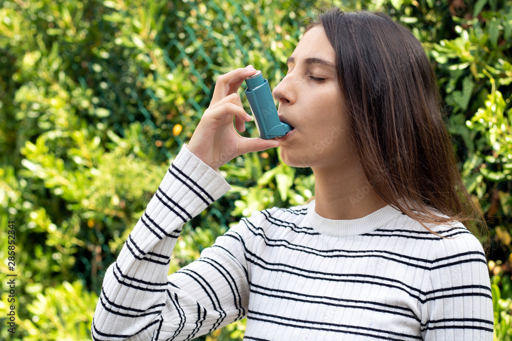 Health and medicine - Young girl using blue asthma inhaler to prevent an asthma attack.