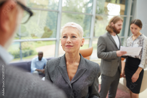 Portrait of mature businesswoman talking to senior colleague while standing in modern office hall  copy space