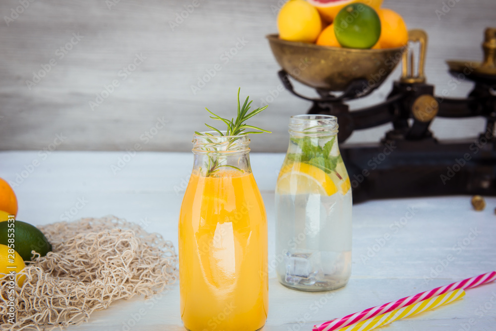 Φωτογραφία Two bottles with homemade lemonade and orange fresh juice with mint and ice on the white wooden background with fresh citrus in vintage scale and some friuts around