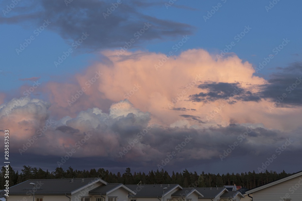 Gorgeous view of beautiful thunder clouds in blue sky above green tree tops.  Roofs of villas, forest, blue sky and clouds converging on the horizon. Beautiful colorful nature background.