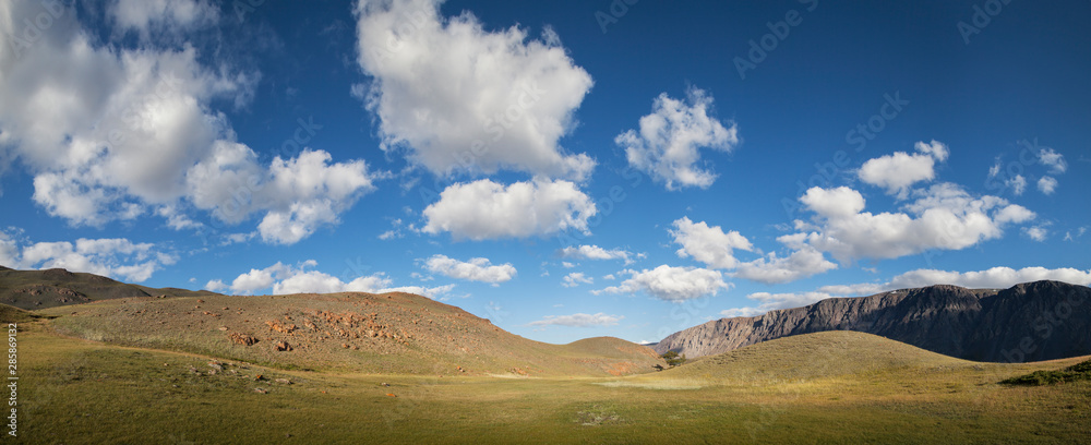 Mountain steppe landscape, wide view. Picturesque blue sky with white clouds.