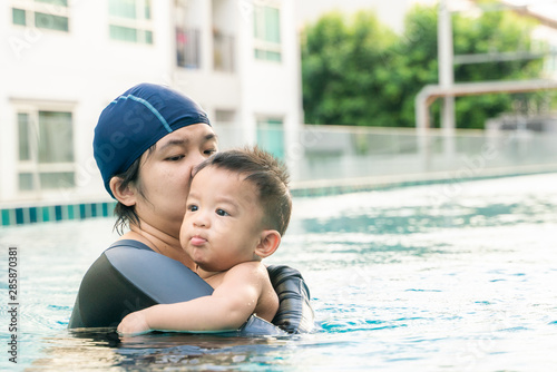 Mother teaching infant 9 month baby boy swimming in pool