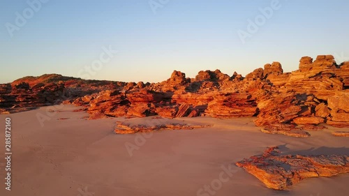 Aerial view of flight along beach at Kimberley coast in outback Western Australia, with red and orange rocks at sunset, blue sky as background and copy space.