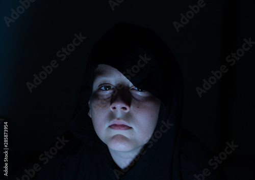 Boy wearing a black hoodie watching a scary movie in the dark 