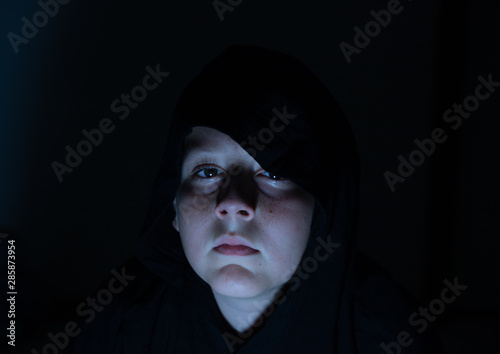 Fotografija Boy wearing a black hoodie watching a scary movie in the dark