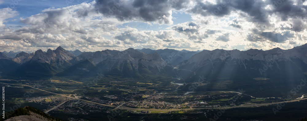 Beautiful Panoramic View of a small city in the Canadian Rocky Mountain Landscape during a cloudy and rainy day. Taken from Mt Lady MacDonald, Canmore, Alberta, Canada.
