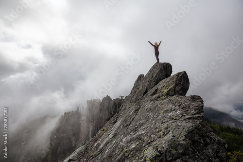 Adventurous Girl with Open Arms on top of a rugged rocky mountain during a cloudy summer morning. Taken on Crown Mountain, North Vancouver, BC, Canada.
