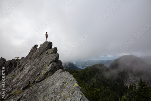 Adventurous Girl Standing on top of a rugged rocky mountain during a cloudy summer morning. Taken on Crown Mountain, North Vancouver, BC, Canada.