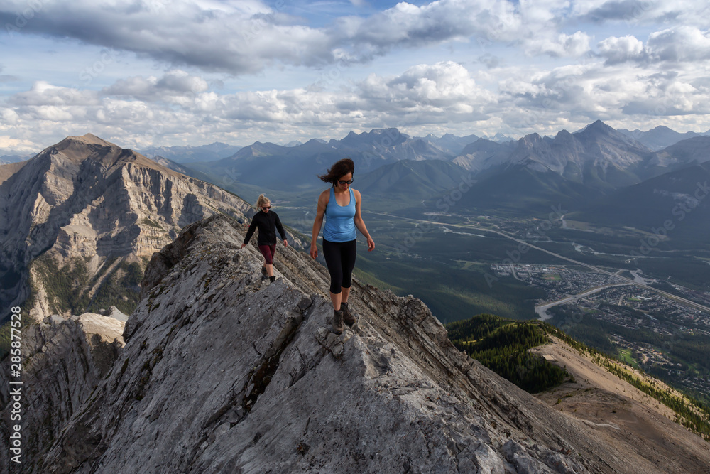 Adventurous Girl is hiking up a rocky mountain during a cloudy and rainy day. Taken from Mt Lady MacDonald, Canmore, Alberta, Canada.