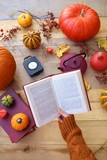 Autumn time. Autumn book sreading . Book in hand, teapot, clock, pumpkins and yellow leaves on a wooden background. Fall season. 