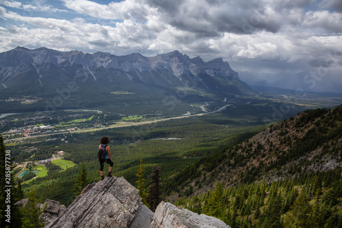 Adventurous Girl is hiking up a rocky mountain during a cloudy and rainy day. Taken from Mt Lady MacDonald, Canmore, Alberta, Canada.