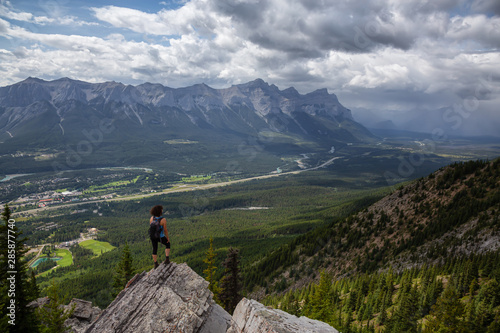 Adventurous Girl is hiking up a rocky mountain during a cloudy and rainy day. Taken from Mt Lady MacDonald, Canmore, Alberta, Canada.