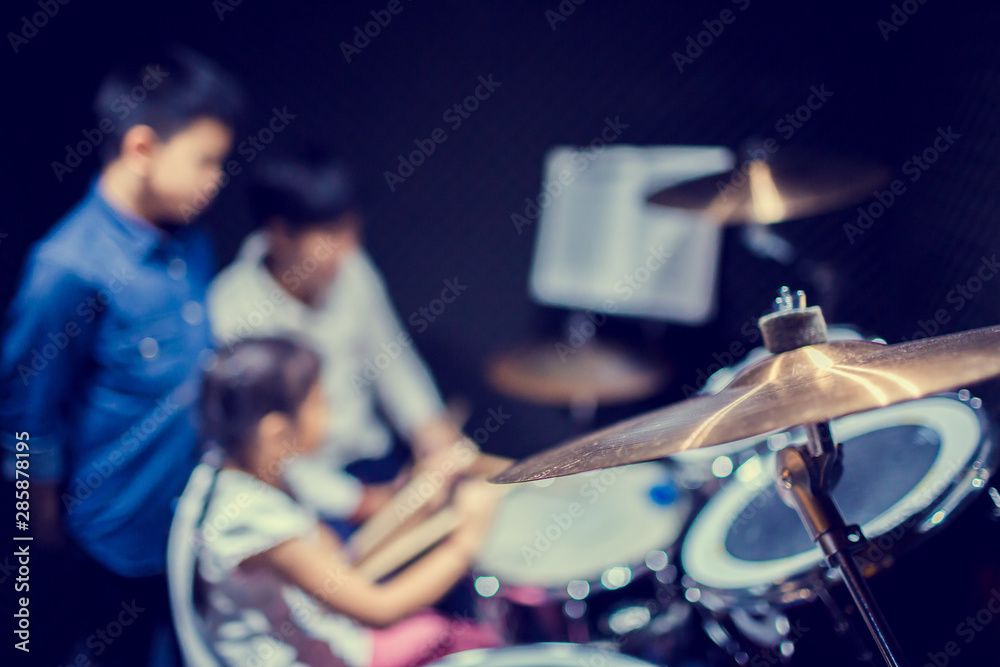 Naklejka premium Selective focus to cymbals of drum set with blurry kid learning and play drum set with teacher in music room. The concept of musical instrument.