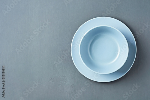 Group of modern empty ceramic plates of blue color lies on dark concrete background. Space for text. Top view