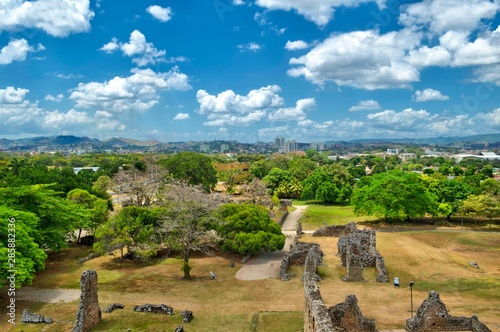 Vista panorámica del horizonte de la ciudad de Panamá. Vista desde el viejo Panamá con una zona boscosa y rocosa en primer plano. Pasto seco y vestigios de las ruinas del viejo Panamá