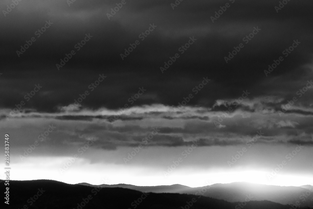 View of dark clouds at sunset, with sun filtering through an hole over the mountain View of dark clouds at sunset, with sun filtering through an hole over the mountain