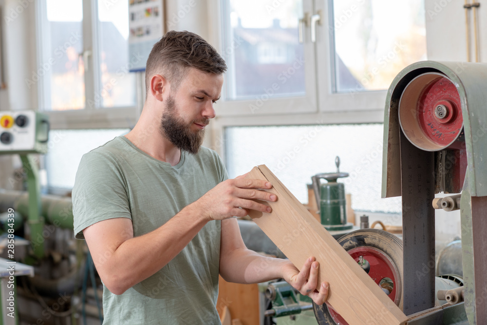 young bearded worker in a carpenter's workshop using grinding machine young bearded worker in a carpenter's workshop using grinding machine