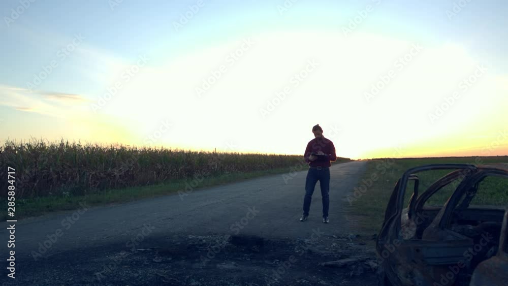 An employee of an insurance company describes a car on the roadside after a fire. Burnt new car. Silhouette of a man and a car outside the city An employee of an insurance company describes a car on the roadside after a fire. Burnt new car. Silhouette of a man and a car outside the city